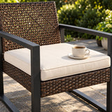 A cup of coffee rests on an ivory cushion of a brown wicker patio chair.